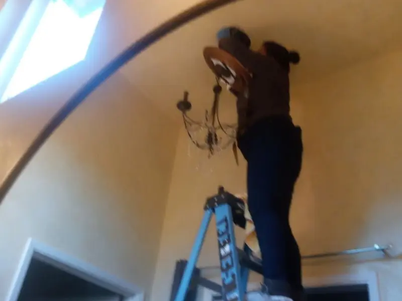 Electrician installing a chandelier in a Thomas residence
